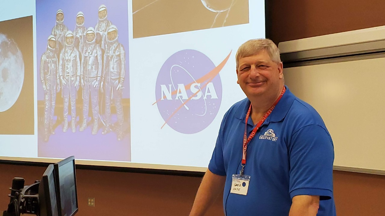 instructor at front of class with projector screen in background 