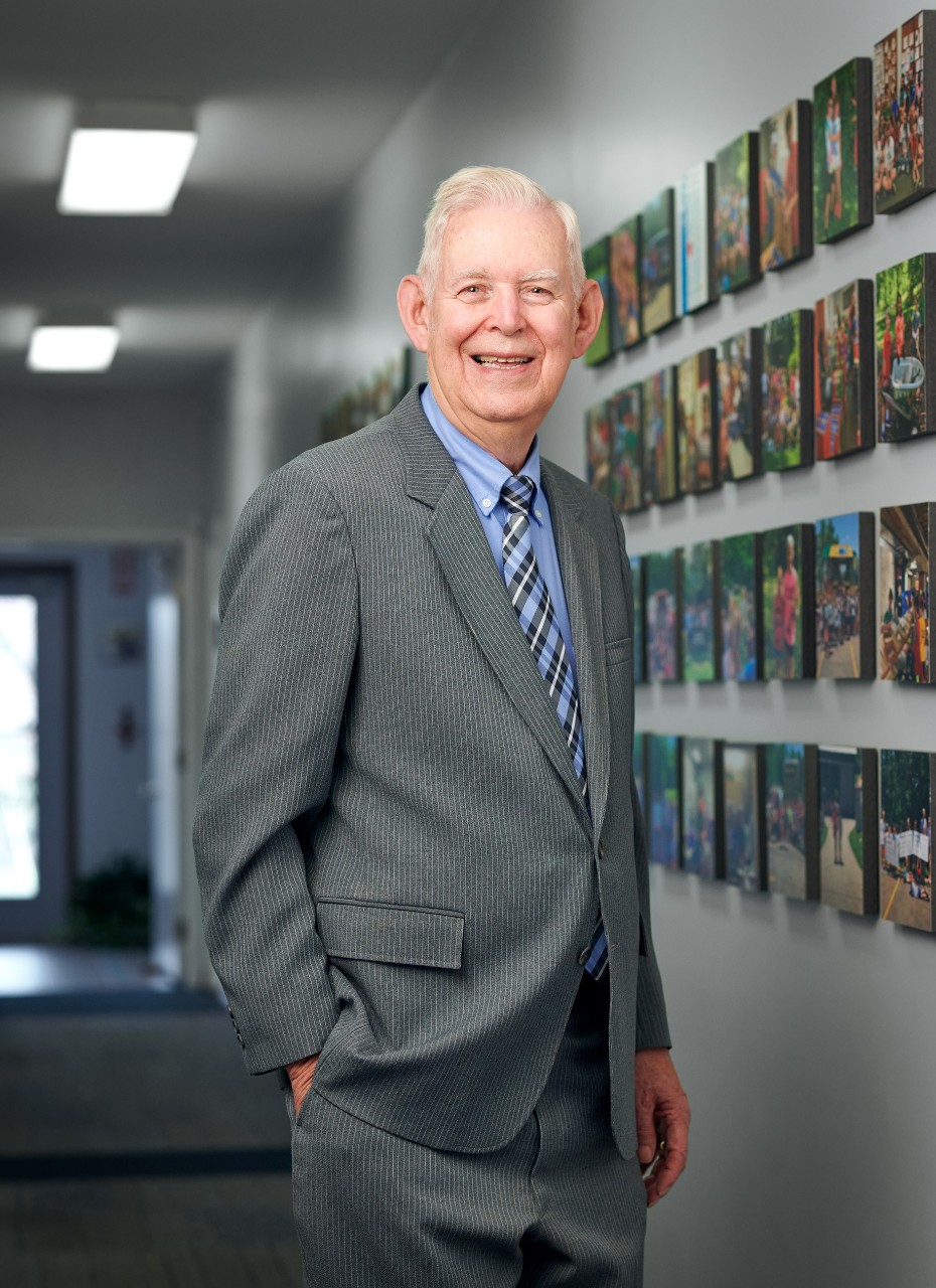 Portrait of Roger Grein in a suit and tie standing in a hallway.